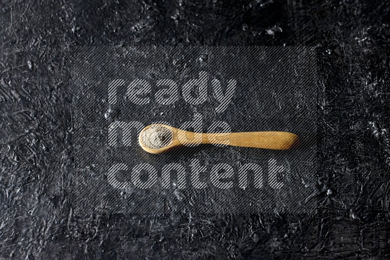 A wooden spoon full of white pepper powder on textured black flooring