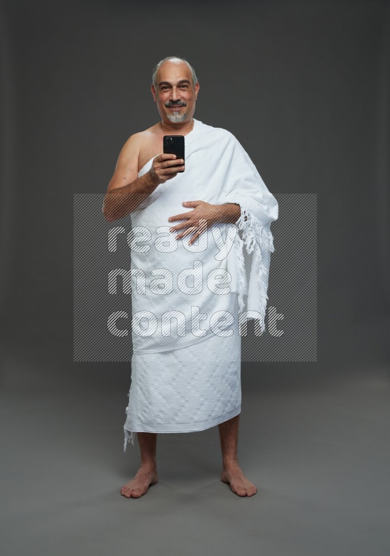 A man wearing Ehram Standing texting on phone on gray background