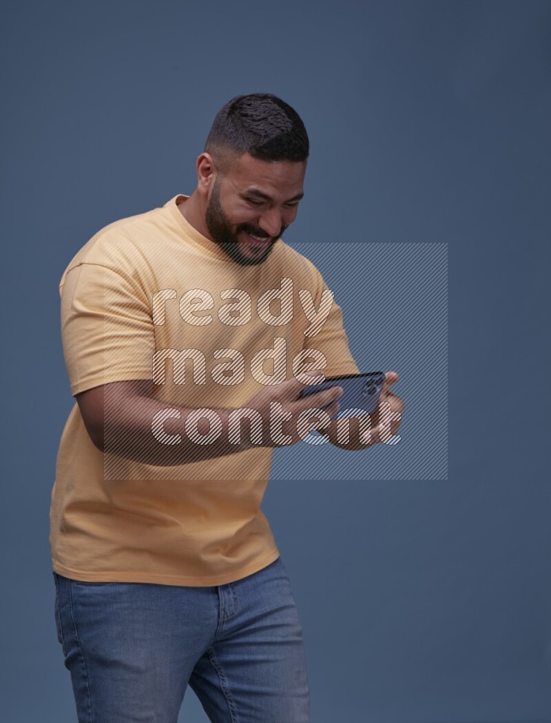 رجل يرتدي بنطال ازرق جينز وقميص اصفر بأكمام قصيره يلعب في جواله