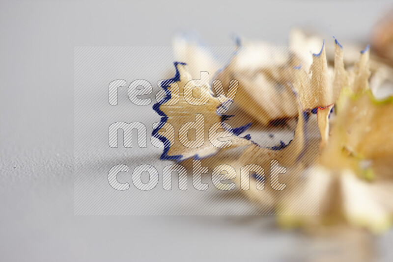 A close-up showing a small pile of pencil shavings with varied color edges on grey background