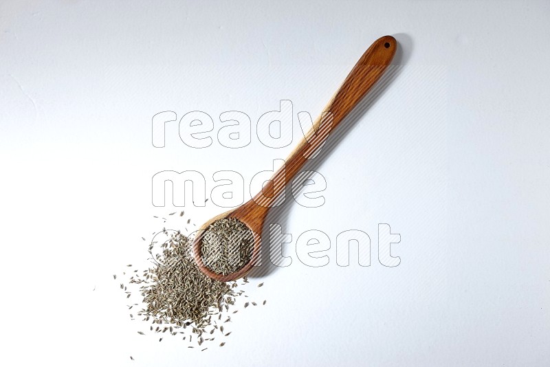 A wooden ladle full of cumin seeds on a white flooring