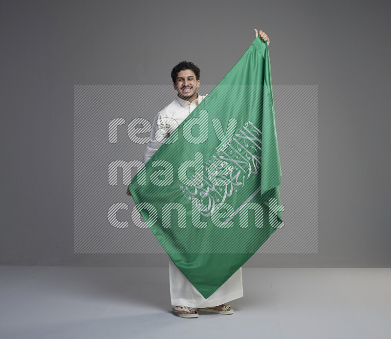 رجل سعودي يرتدي ثوب ويحمل علم السعودية