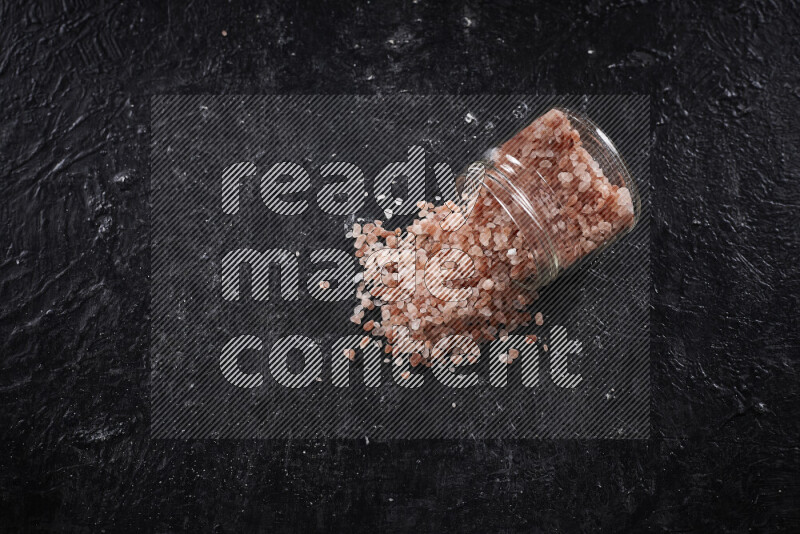 A glass jar full of coarse himalayan salt crystals on black background