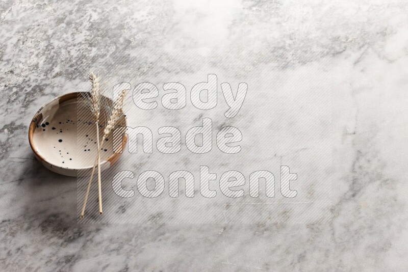 Wheat stalks on multicolored pottery bowl on grey marble background