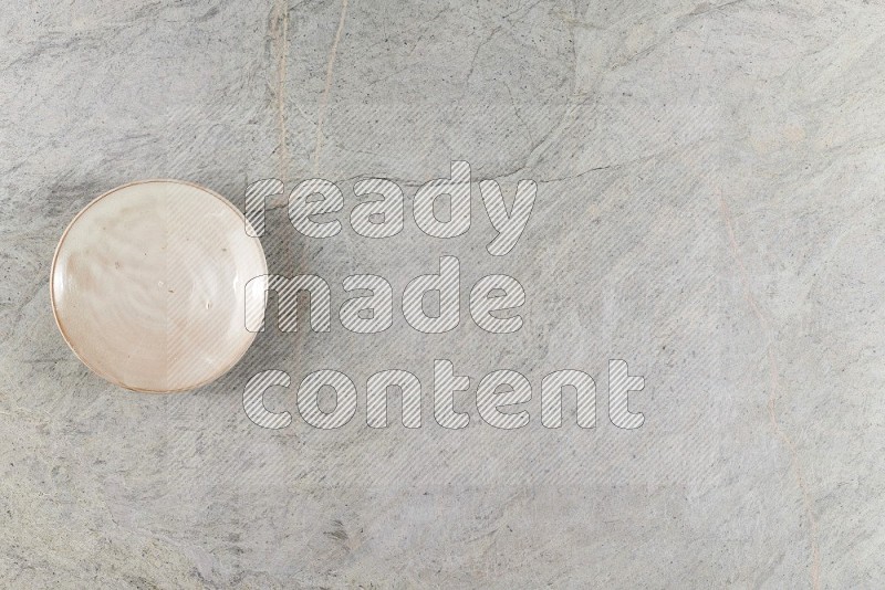 Top View Shot Of A Beige Pottery Plate On Grey Marble Flooring