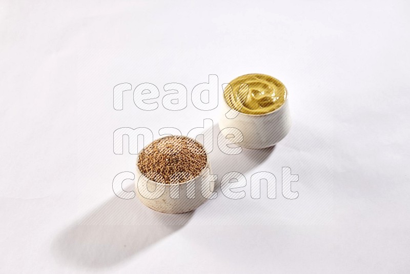 2 beige pottery bowls full of mustard seeds and mustard paste on white flooring in different angles