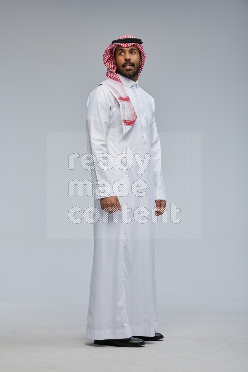 Saudi man Wearing Thob and shomag standing interacting with the camera on Gray background