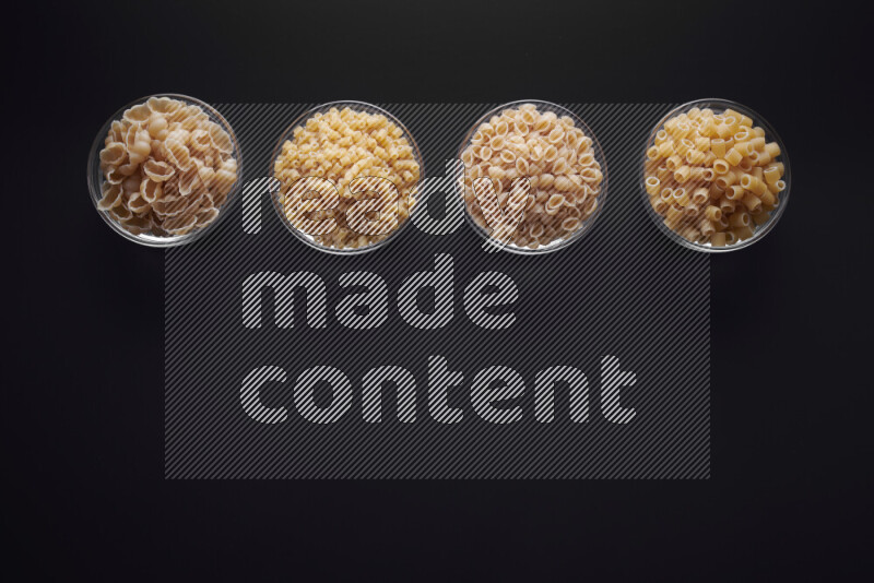 Different pasta types in glass bowls on black background