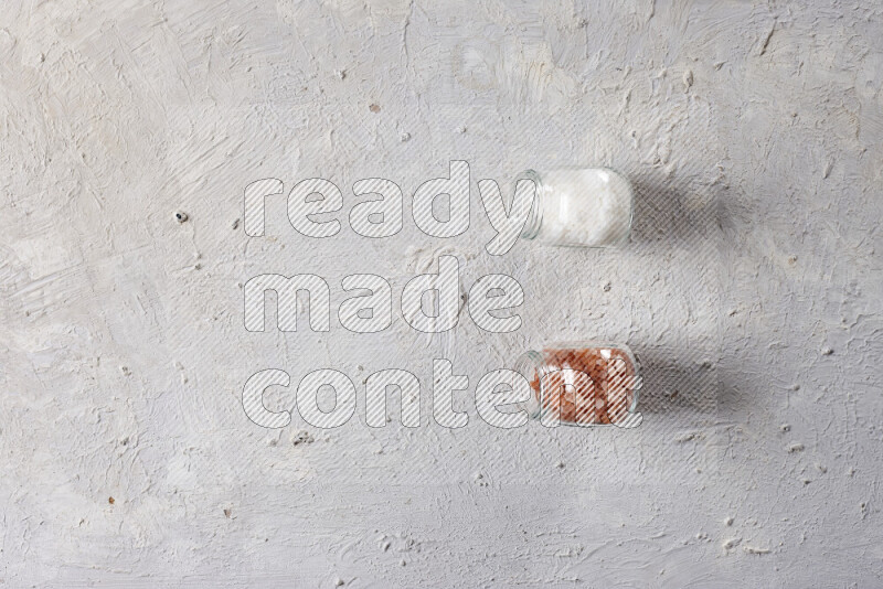 2 glass jars one is filled with coarse himalayan salt and the other with coarse sea salt on white background