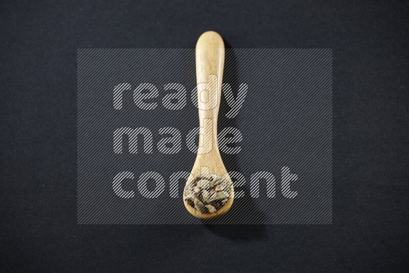 A wooden spoon full of cardamom on black flooring