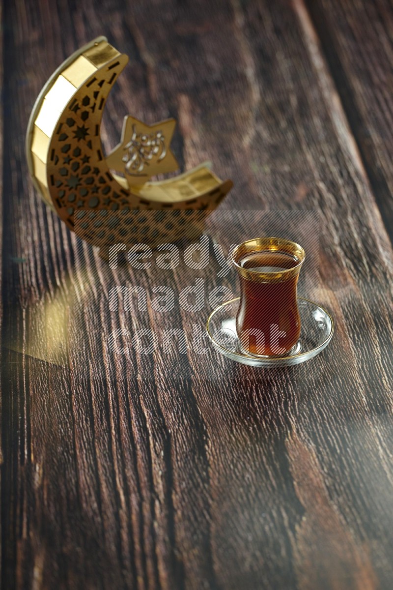 فانوس خشبي هلالي باللون الذهبي مع مشروبات مختلفة وتمر ومكسرات وسبحة صلاة وقرآن على خلفية خشبية بنية