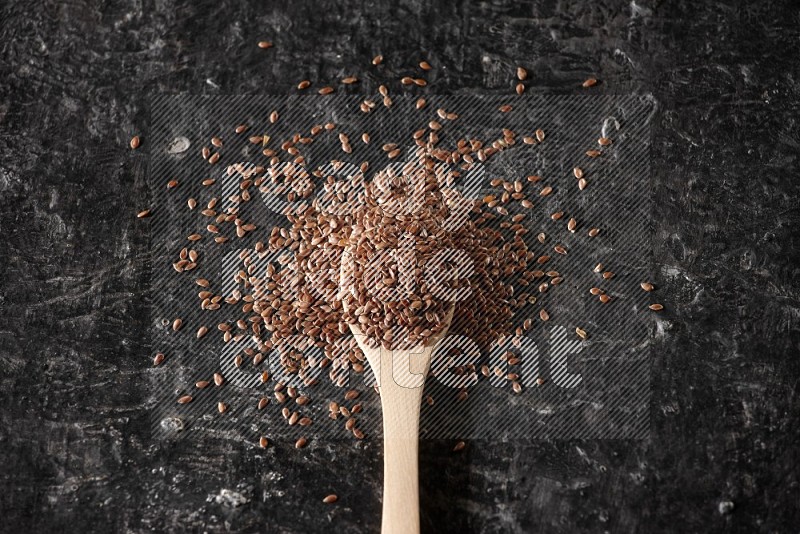 A wooden spoon full of flax and surrounded by seeds on a textured black flooring in different angles