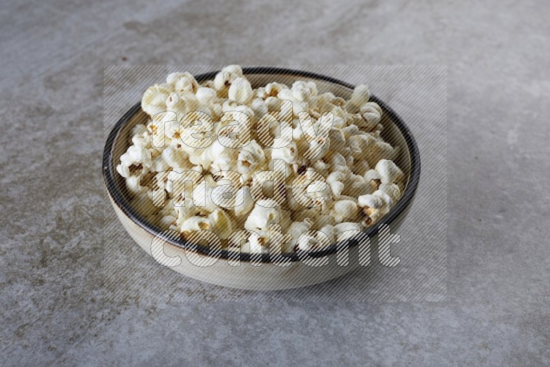 popcorn in a multi-colored pottery bowl on a grey textured countertop