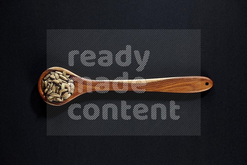 A wooden ladle full of cardamom on black flooring