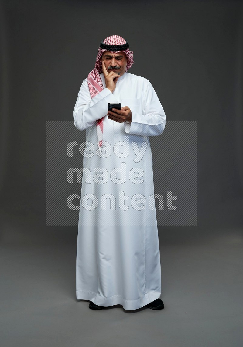 Saudi man with shomag Standing texting on phone on gray background