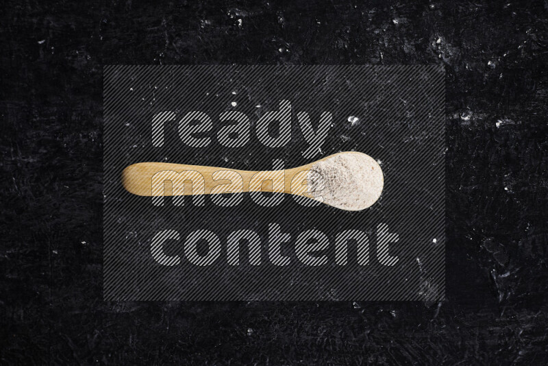 A wooden spoon full of onion powder on black background