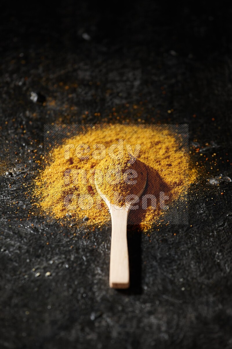 A wooden spoon full of turmeric powder on textured black background