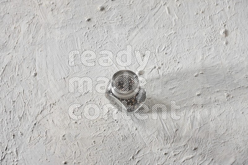 حبوب الفلفل الأسود في وعاء زجاجي علي خلفية بيضاء