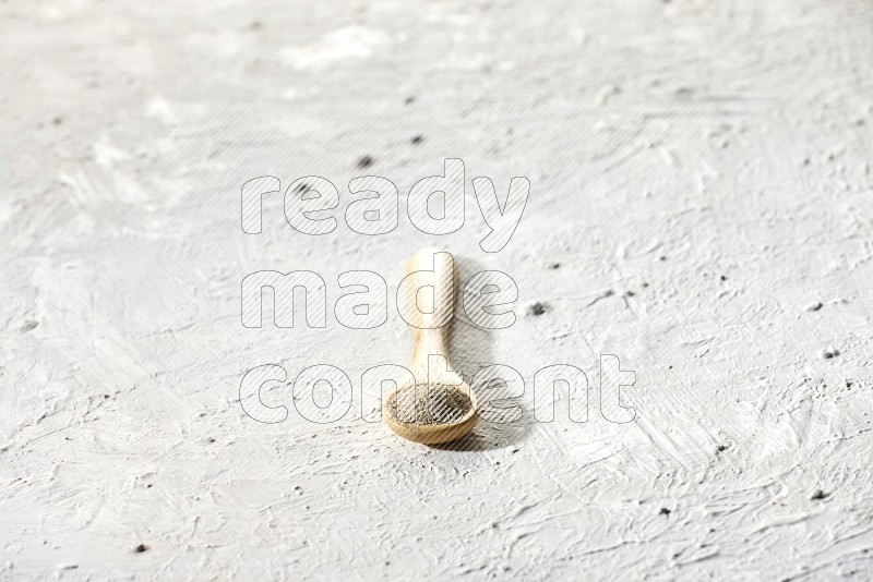 A wooden spoon full of white pepper powder on textured white flooring