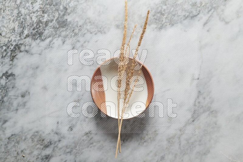 Wheat stalks on multicolored pottery plate on grey marble background