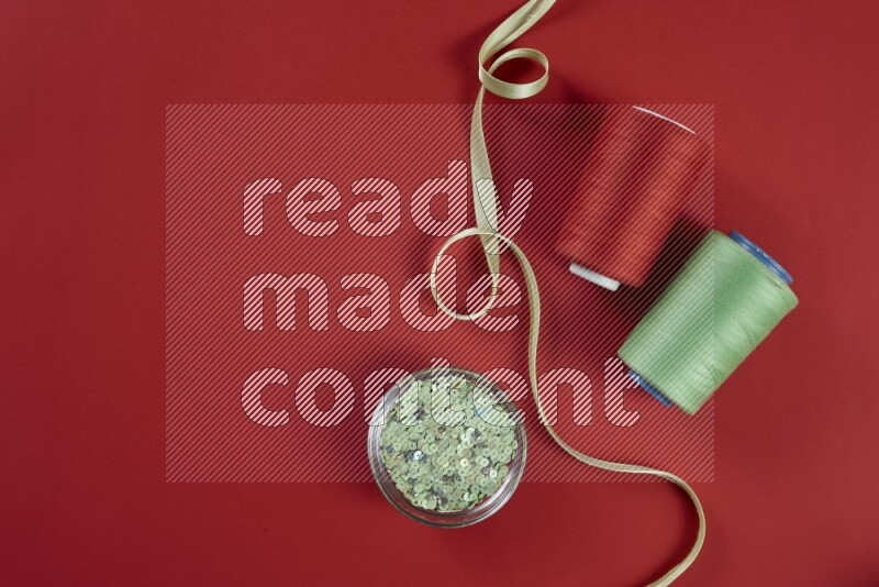 A green and red collection of sewing and tailoring tools arranged on a red background