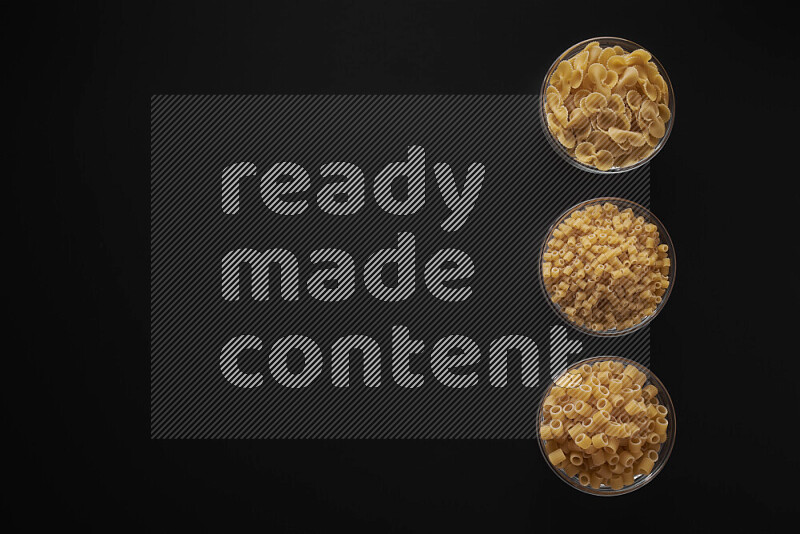 Different pasta types in 3 glass bowls on black background