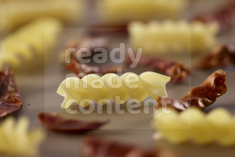Raw pasta with different ingredients such as cherry tomatoes, garlic, onions, red chilis, black pepper, white pepper, bay laurel leaves, rosemary and cardamom on beige background
