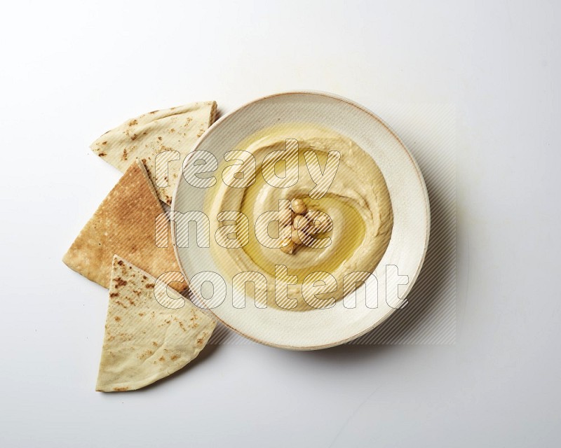 Hummus in a pottry plate garnished with roasted chickpeas on a white background