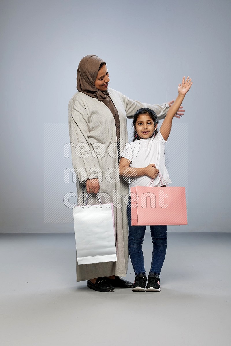 Mom and daughter holding shopping bags on gray background