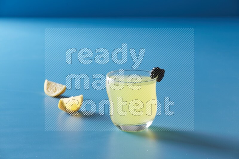 glass of lemon juice with berry on blue background
