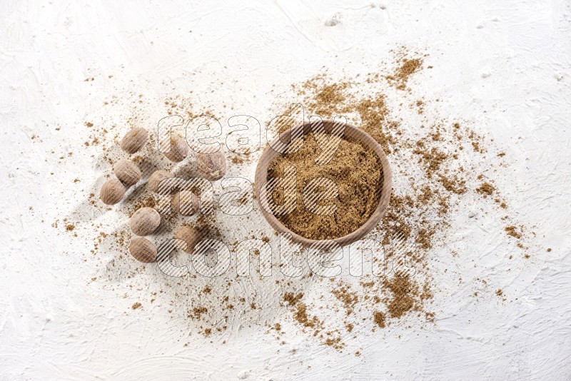 A wooden bowl full of nutmeg powder with the seeds and sprinkled powder beside it on a textured white flooring in different angles