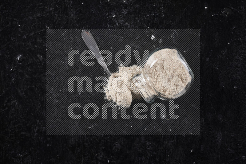 A glass jar full of onion powder flipped with some spilling powder on black background