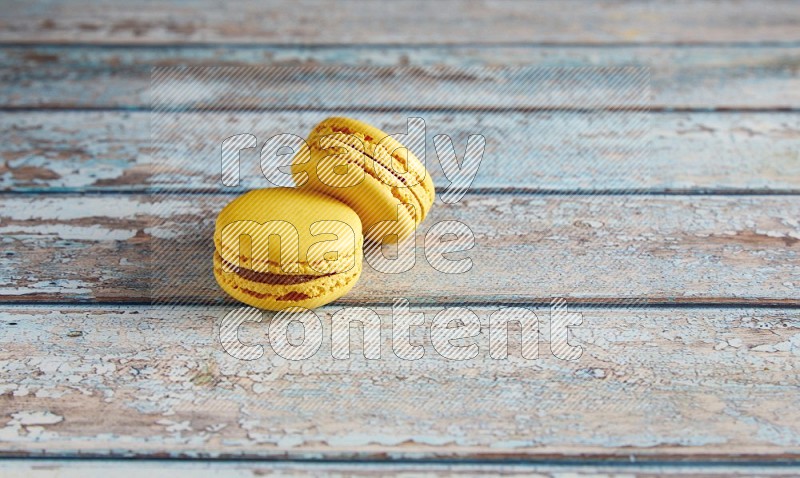 45º Shot of two Yellow Lemon macarons on light blue wooden background