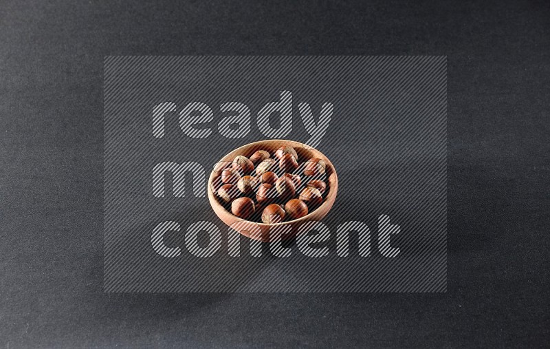 A wooden bowl full of hazelnuts on a black background in different angles