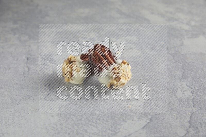 Two pecan stuffed date covered with white chocolate and chopped walnuts on alight grey background