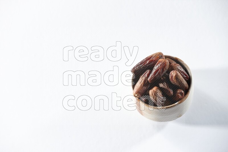 A beige ceramic bowl full of dried dates on a white background in different angles