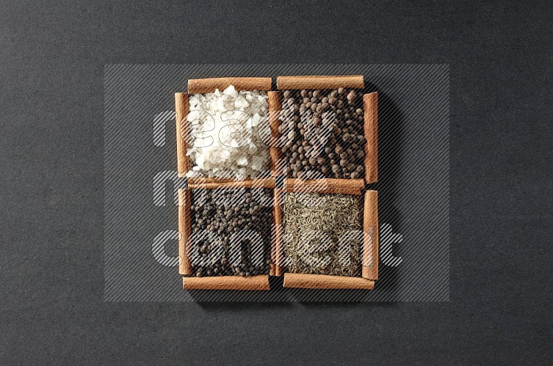 4 squares of cinnamon sticks full of black pepper, cumin, allspice and white salt on black flooring