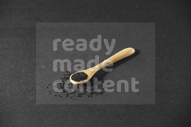 A wooden spoon full of black seeds and seeds spread beside it on a black flooring
