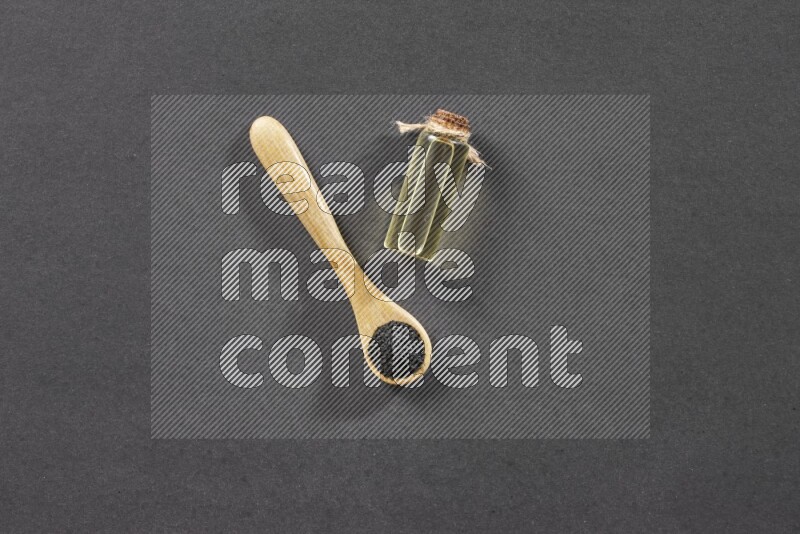 A wooden spoon full of black seeds and a glass bottle of black seeds oil on a black flooring