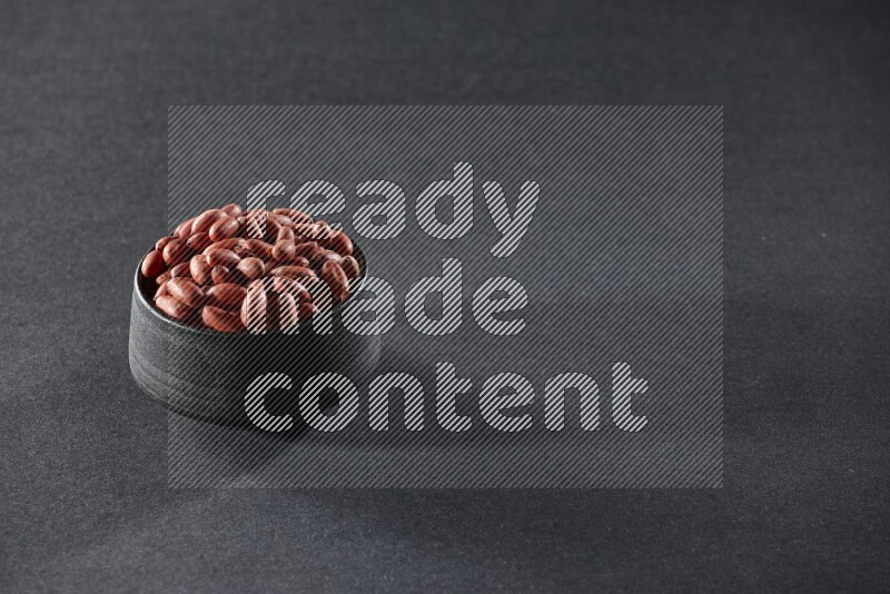A black pottery bowl full of red skin peanuts on a black background in different angles