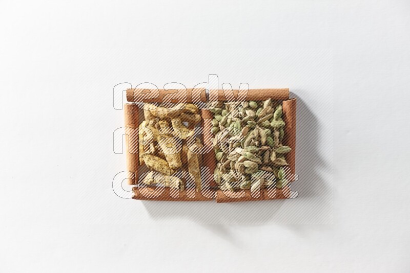 مربعان من أعواد القرفة ممتلئان بحبوب الهيل وأصابع الكركم علي خلفية بيضاء