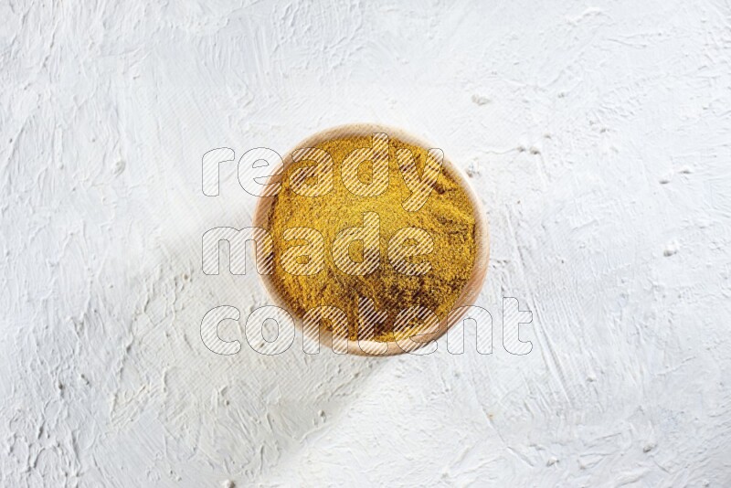 A wooden bowl full of turmeric powder on a textured white flooring