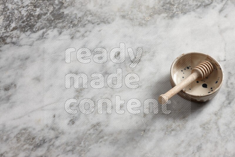 وعاء فخاري متعدد الألوان مع ملعقة عسل خشبية بداخله على خلفية من الرخام الرمادي