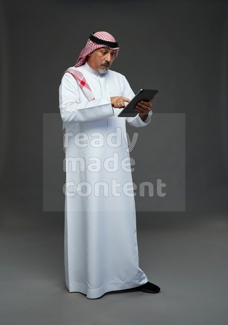 Saudi man with shomag Standing working on tablet on gray background