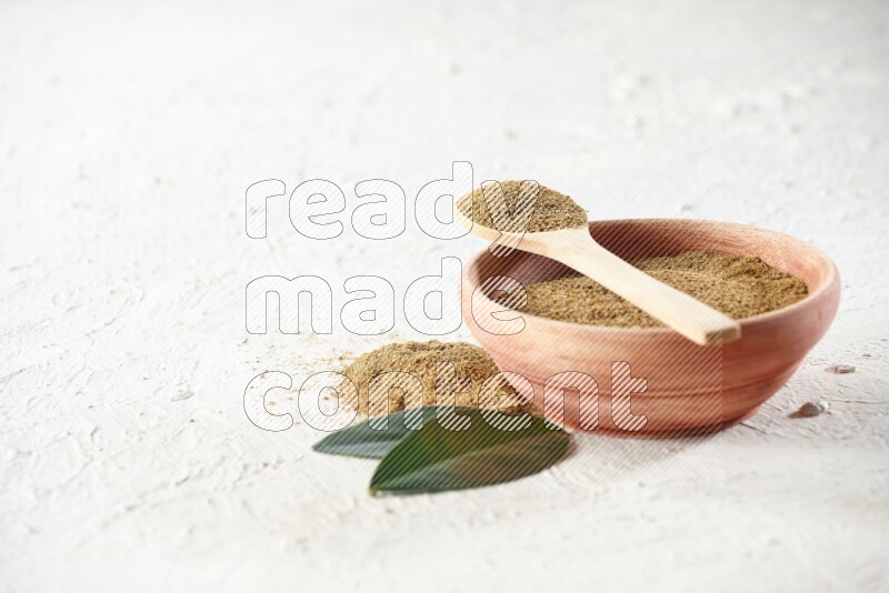 A wooden bowl and wooden spoon full of cumin powder on textured white flooring