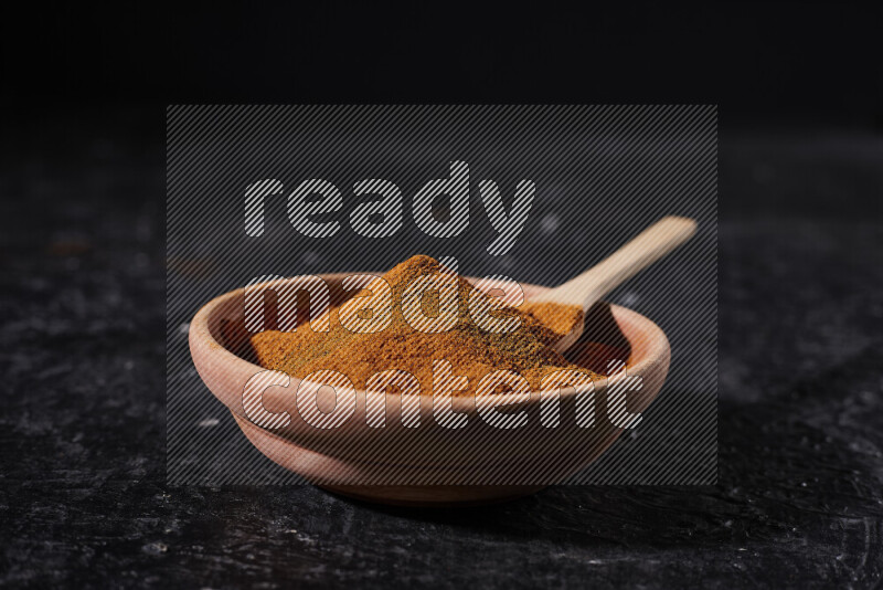 A wooden bowl full of ground paprika powder and a wooden spoon in it on black background