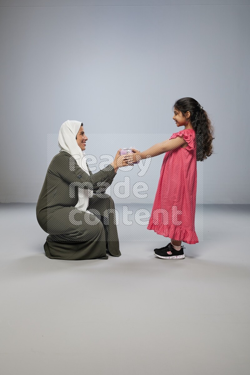 A girl giving a gift to her mother on gray background