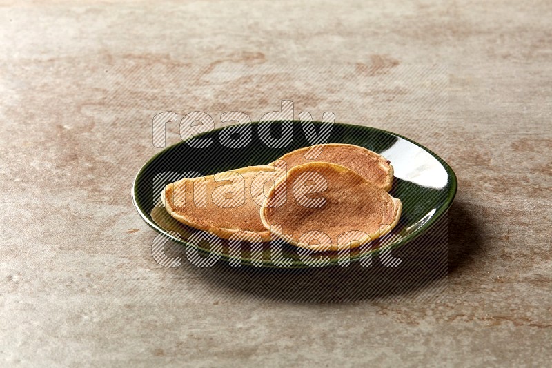 Three stacked plain mini pancakes in a green plate on beige background