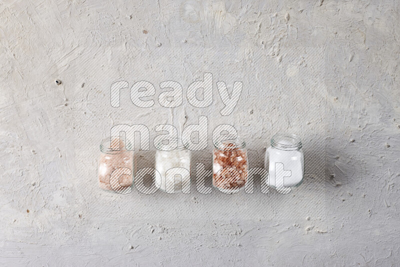 4 glass jars filled with table salt, coarse sea salt, fine himalayan salt and coarse himalayan salt on white background