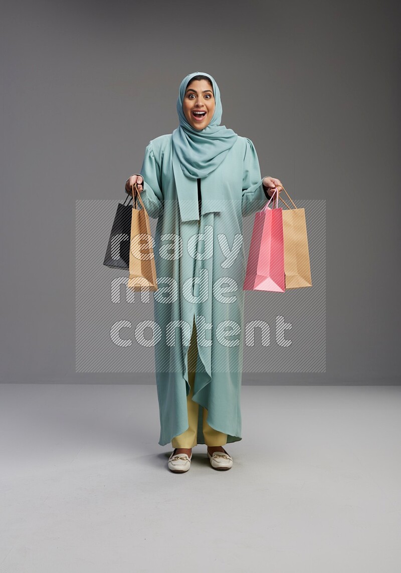 Saudi Woman wearing Abaya standing holding shopping bag on Gray background